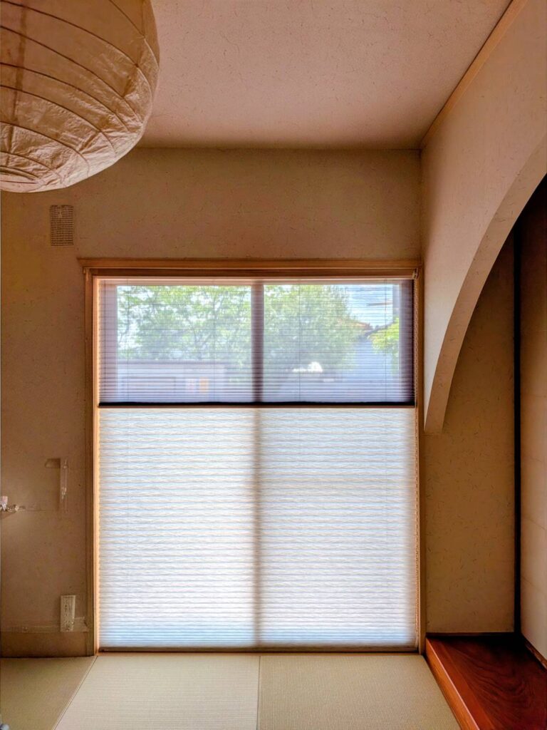 施工後の和室。上部がレース、下部が不透明生地になったタチカワブラインドのプリーツスクリーン「ペルレゆらぎ（ペアタイプ）」が、窓枠内にスッキリと天付けされた写真。上から自然光が差し込んでいる。
