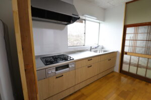 LIXILのシステムキッチン「シエラS」の斜め全体写真。木目調の扉と、広くなった手前の通路スペースが確認できる。